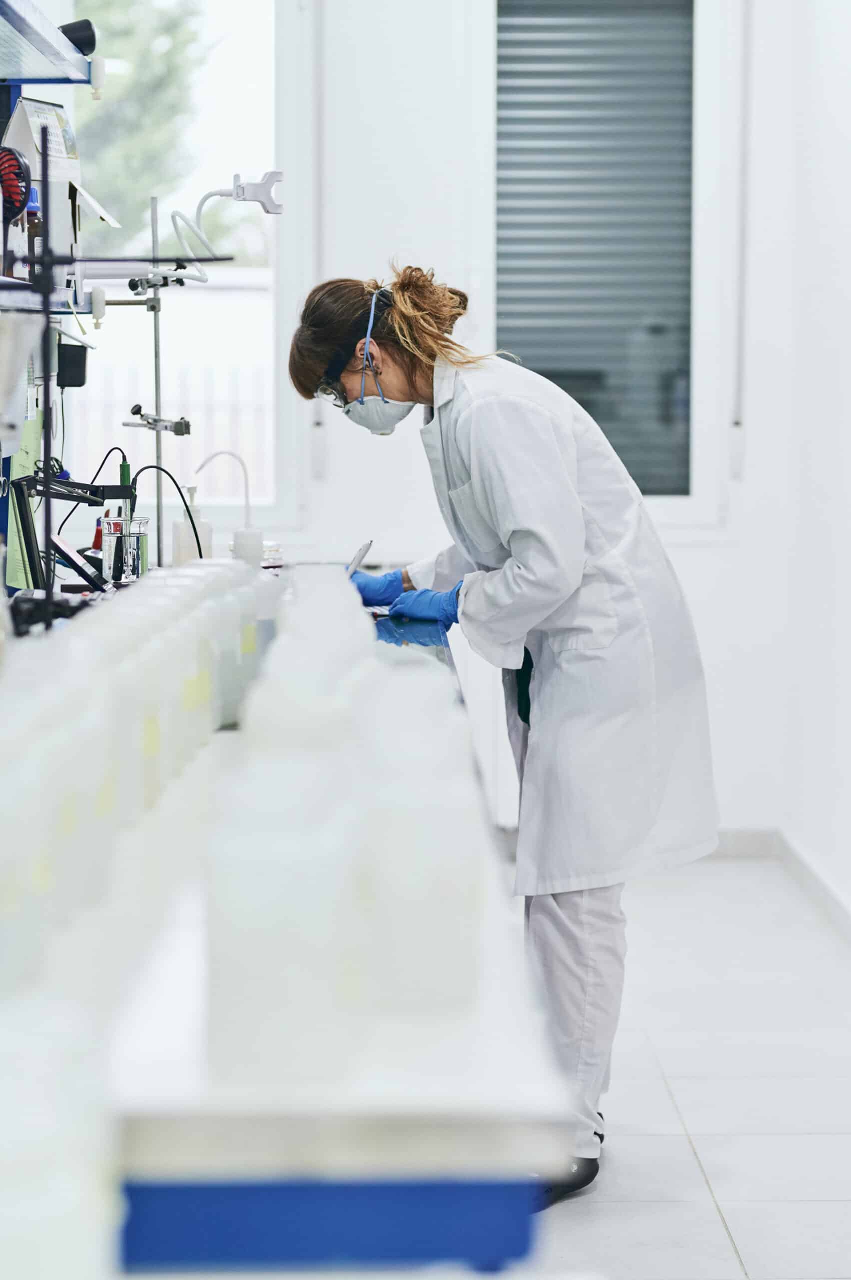 a female scientist working in a lab that abides by good laboratory practises takes notes about lab samples
